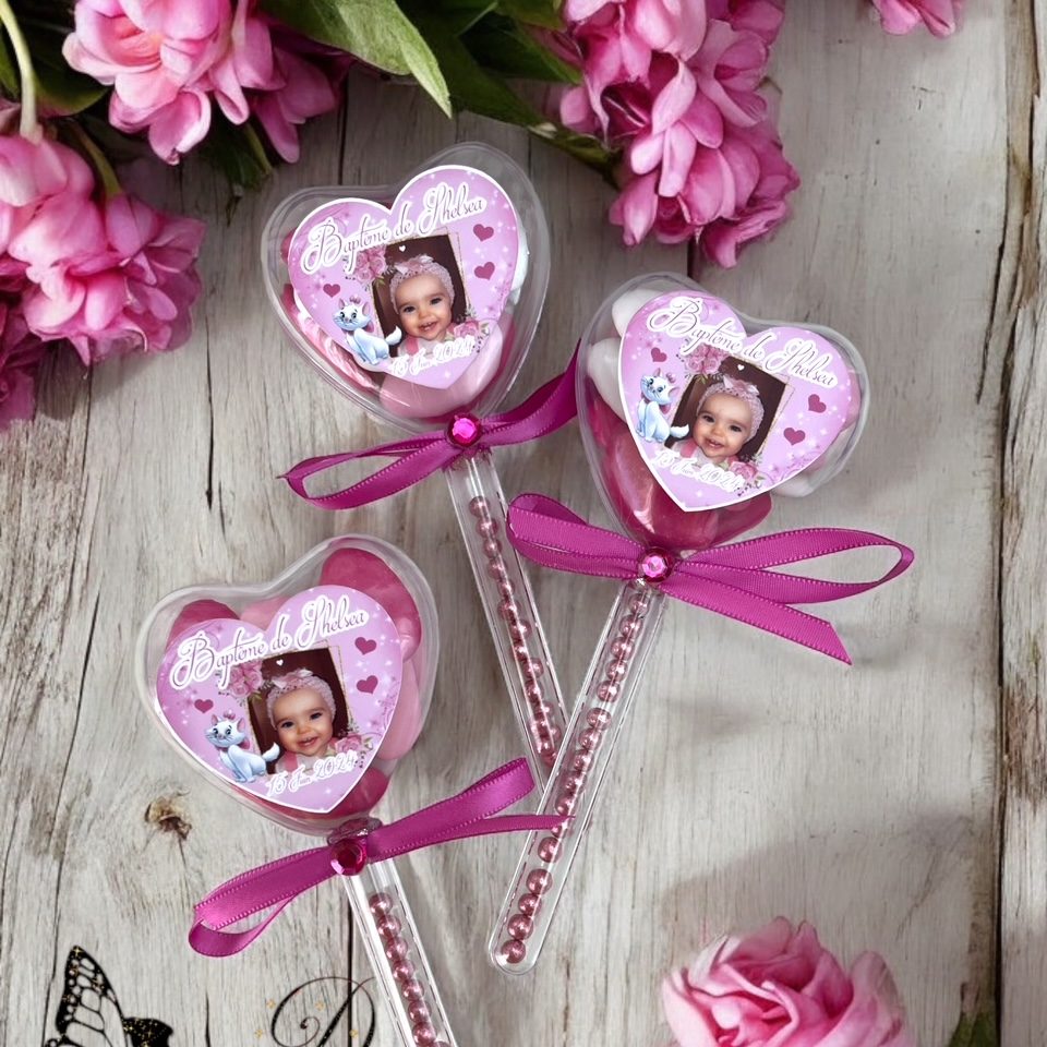 baguette dragées cœur Trois sucettes en forme de cœur avec des images d'enfants et des rubans roses.